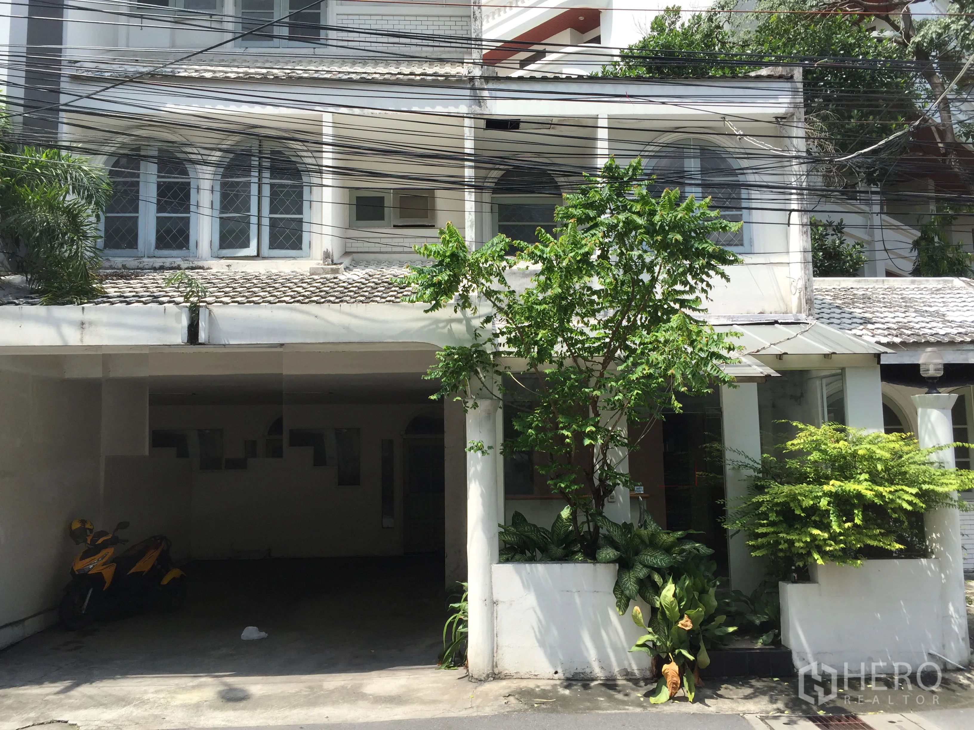 Retail Space for rent in Watthana, Bangkok - Street-facing white low-rise building with arched windows, a covered carport, and leafy planters, ideal for retail near BTS Thonglor.