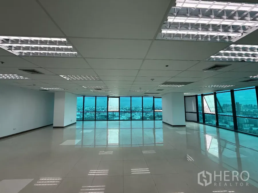 办公空间 出租在Huai Khwang, Bangkok - 开放式办公楼层，落地窗与城市天际线视野，瓷砖地面与网格吊顶灯。