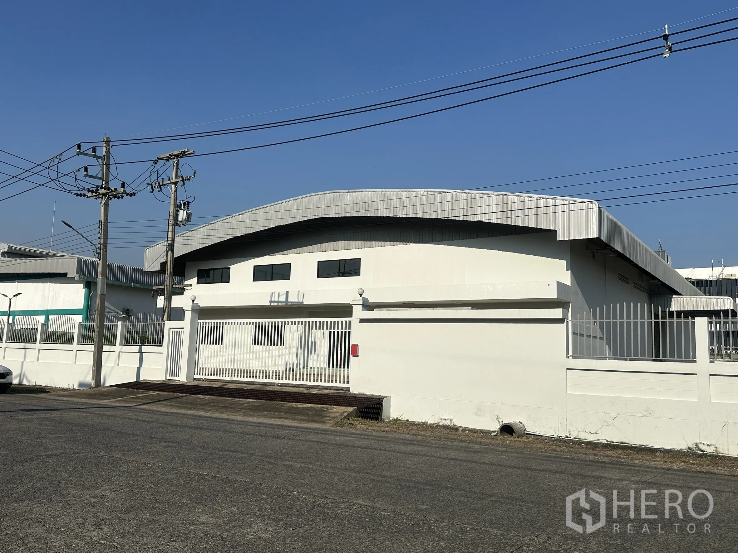 工厂 for sale in Khlong Luang, Pathum Thani - 白色厂房外观，弧形金属屋顶与临街大门。