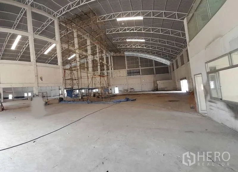 Factory for rent in Mueang Samut Prakan, Samut Prakan - Open warehouse hall with arched roof, scaffolding and expansive concrete floor.