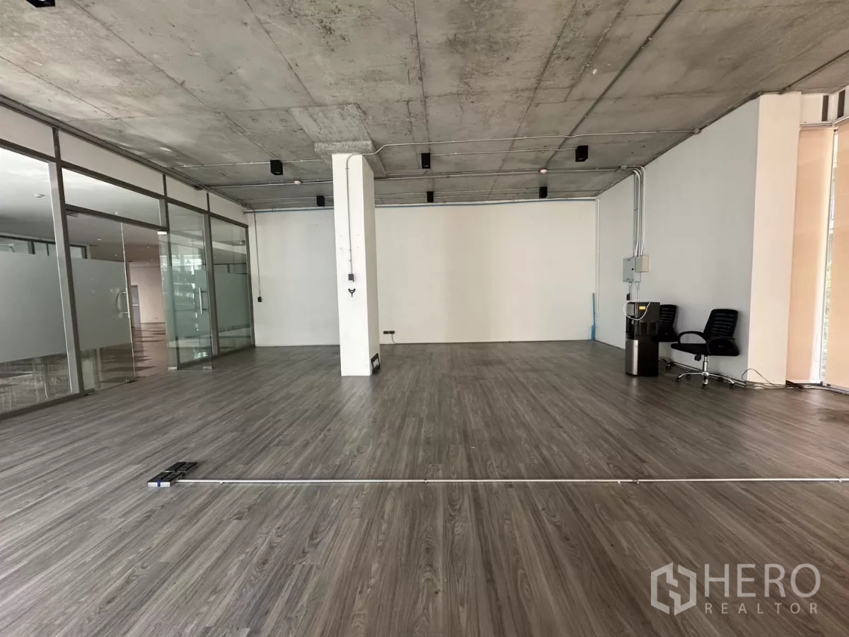 Retail Space for rent - Deep interior shot showing wide plank floors, white feature wall, visible conduits, and glass wall to the corridor.