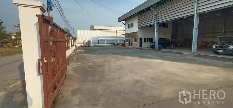 Warehouse for rent in Khlong Luang, Pathum Thani - Sliding gate opening to a large concrete yard offering easy truck turning and access to loading bays.