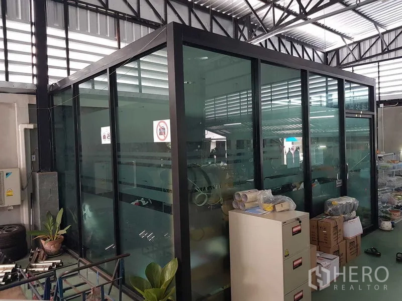Warehouse for sale in Lam Luk Ka, Pathum Thani - Glass-walled office cabin inside the warehouse under a steel truss roof.