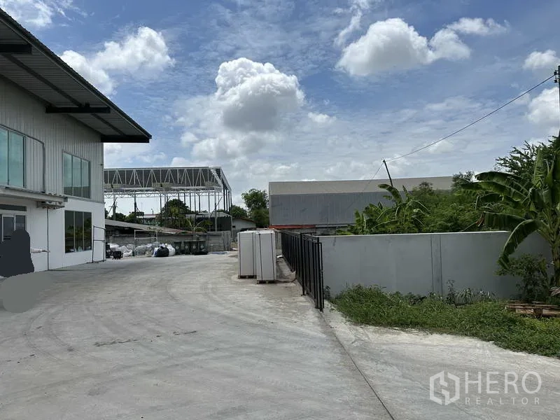Warehouse for rent in Lat Krabang, Bangkok - Wide concrete driveway beside an office block leading to the warehouse, with perimeter wall and greenery.