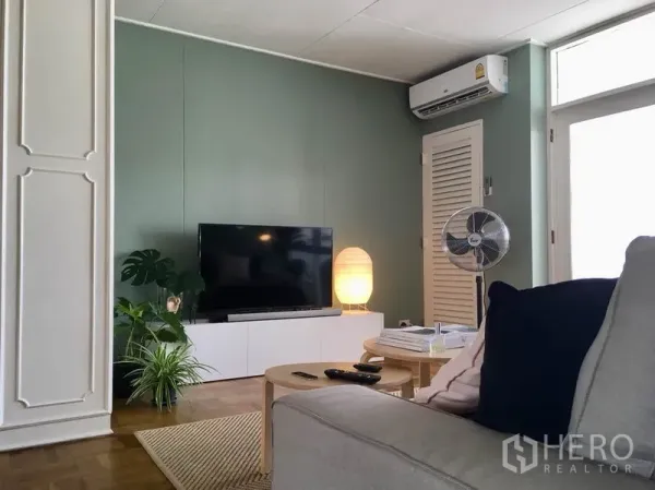 房间 出租在Khlong Toei, Bangkok - 客厅影音墙，平板电视、收纳柜与柔和台灯，配备空调。
