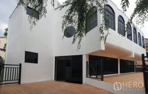 Home Office for rent or sale in Bang Na, Bangkok - Side angle of the white exterior with arched windows and an expansive wooden terrace.