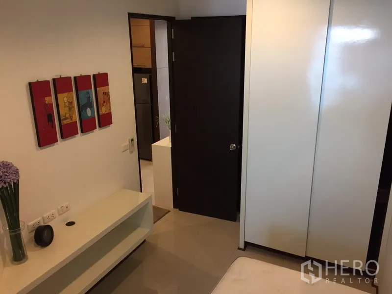 Condominium for rent in Khlong Toei, Bangkok - Second bedroom interior with glossy wardrobe, wall art and doorway to hall.