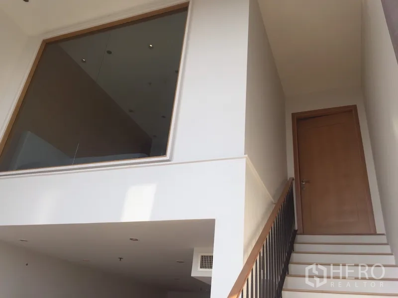 Condominium for rent in Khlong Toei, Bangkok - Staircase leading to the upper level with interior glass panel and wooden door.
