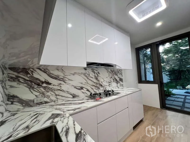 Townhouse for rent in Phra Khanong, Bangkok - Modern closed kitchen with marble-pattern counters, gas hobs and garden outlook.