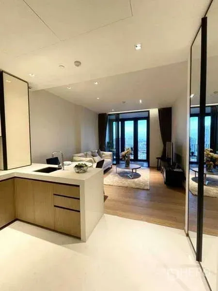 Condominium for rent or sale in Khlong Toei, Bangkok - Open-plan living area with modern kitchenette, wood floors, and balcony doors facing a city view.