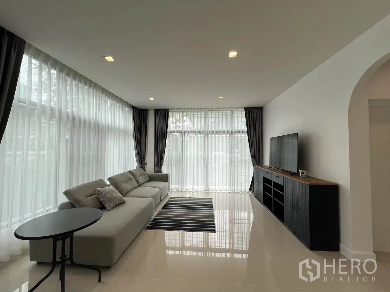 Detached House for rent in Bang Kapi, Bangkok - Bright living room with large L-shaped sofa, TV console and sheer curtains.