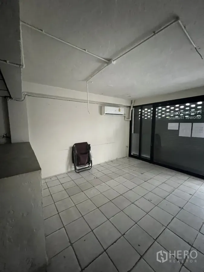Shophouse for rent in Suan Luang, Bangkok - Ground-floor tiled room with wall air conditioner and sliding glass storefront.