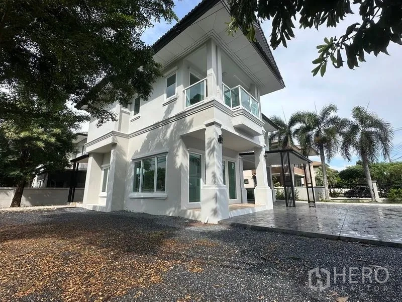 Detached House for sale in Lam Luk Ka, Pathum Thani - Corner exterior view of the white two-storey house with balconies and driveway.