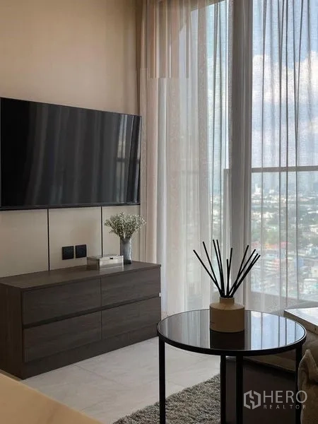 Condominium for rent in Pathum Wan, Bangkok - Living area with wall-mounted TV, low console and full-height window.