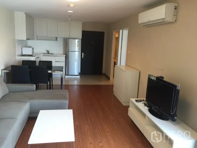 Condominium for rent in Huai Khwang, Bangkok - Open-plan living area with sofa, TV console, air conditioner and kitchen with fridge.
