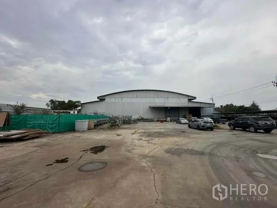 Factory for rent in Pathum Thani - Wide exterior view of a large steel factory with expansive concrete yard and parking.
