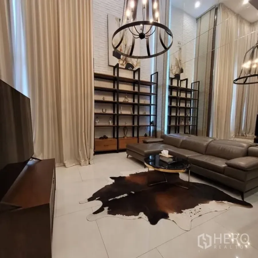 Condominium for rent in Khlong Toei, Bangkok - Cozy living space with tall shelves, round coffee table, and chandelier under a high ceiling.