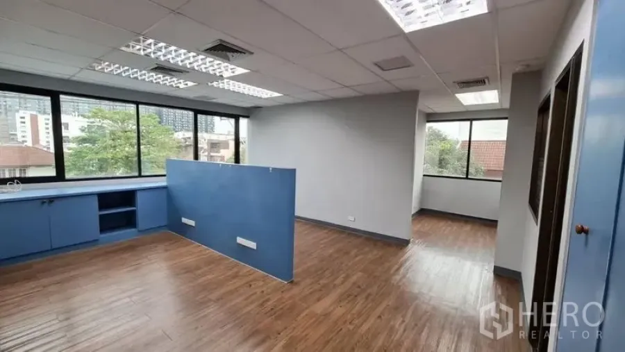 Office Space for rent in Watthana, Bangkok - Bright open-plan office with wood floors, blue built-ins and large windows overlooking Sukhumvit.
