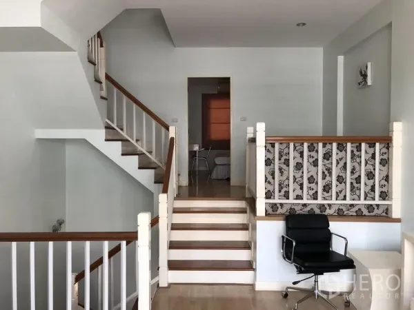 Townhouse for rent in Prawet, Bangkok - Split-level landing with wooden stairs, white railings and a small workspace.