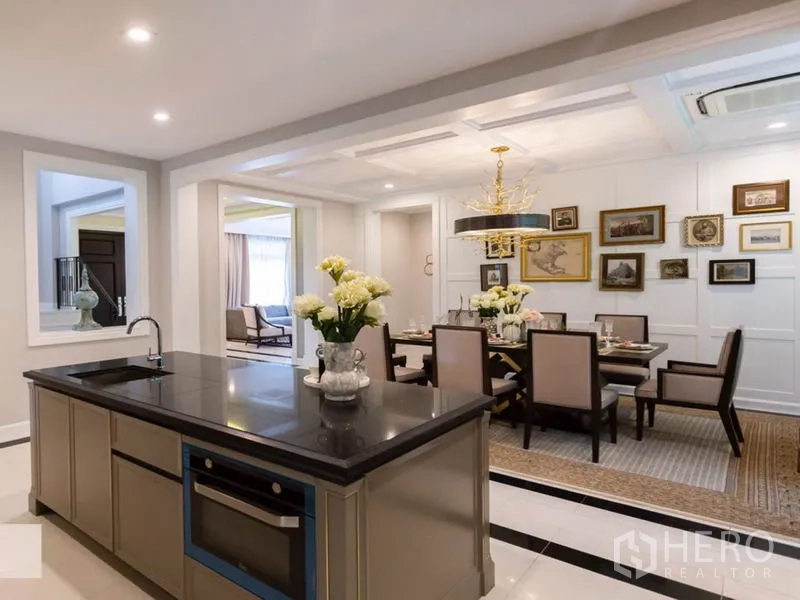 Detached House for rent in Mueang Samut Prakan, Samut Prakan - Modern open kitchen with black stone island facing an elegant dining area decorated with framed art.