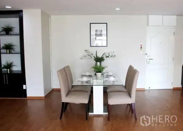 Condominium for rent in Khlong Toei, Bangkok - Dining area for four with glass table, upholstered chairs and open shelving.