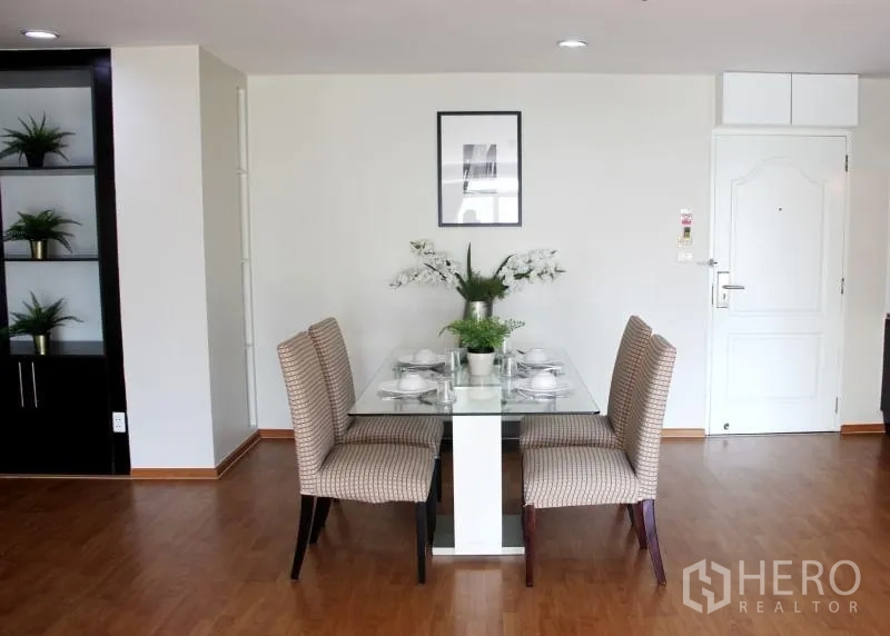Condominium for rent in Khlong Toei, Bangkok - Dining area for four with glass table, upholstered chairs and open shelving.
