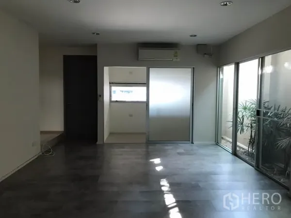 Townhouse for rent in Suan Luang, Bangkok - Bright living area with dark flooring, air conditioning and a sliding door to a small room and light well.