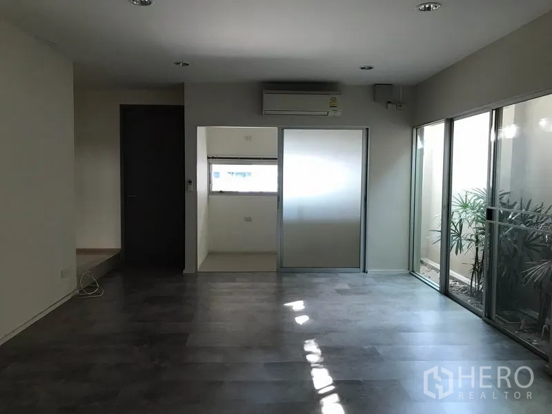 Townhouse for rent in Suan Luang, Bangkok - Bright living area with dark flooring, air conditioning and a sliding door to a small room and light well.
