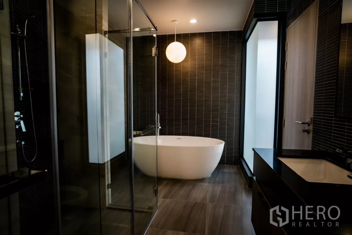 Detached House for rent or sale in Bang Kapi, Bangkok - Luxury bathroom with freestanding oval bathtub, glass shower and dark tiles.