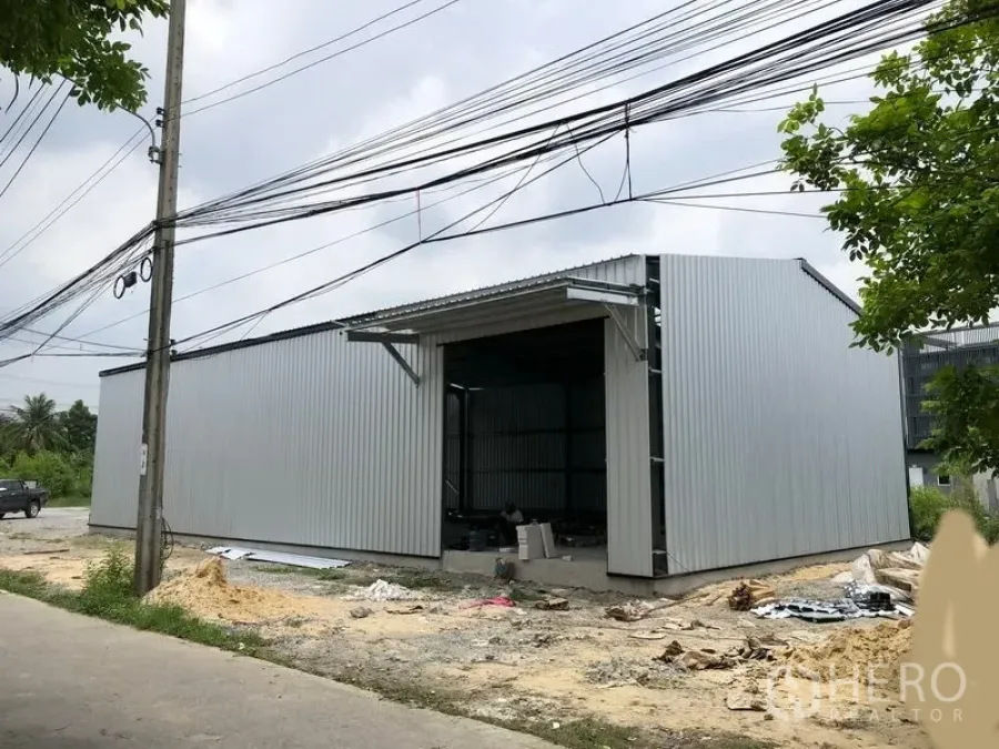 Warehouse for rent in Bang Yai, Nonthaburi - Corrugated metal warehouse exterior with wide loading door and roadside access in Bang Yai.