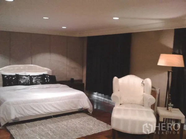 Townhouse for rent in Khlong Toei, Bangkok - Large master bedroom with king bed, comfy armchair, floor lamp and dark blackout curtains.