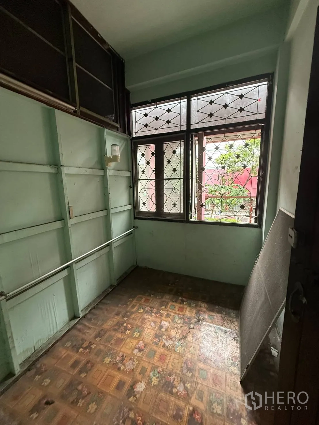 Shophouse for rent in Khlong Toei, Bangkok - Compact room with mint walls, patterned flooring, and grilled windows.
