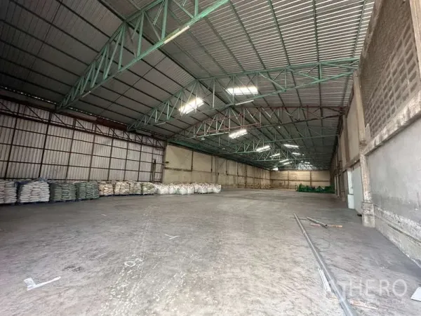 Warehouse for rent in Mueang Pathum Thani, Pathum Thani - Open storage hall with concrete flooring, green steel beams, and side loading area.