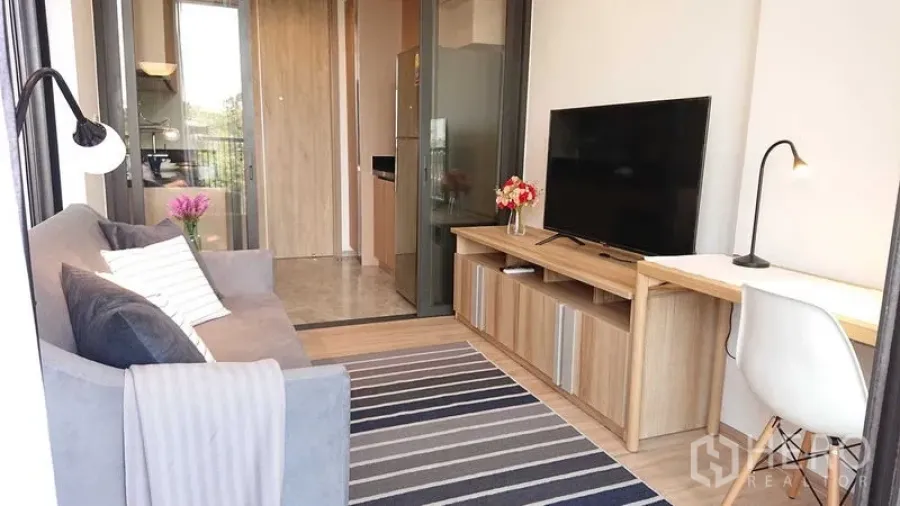 Condominium for sale in Watthana, Bangkok - Living room perspective toward the kitchen with TV console, desk and sliding glass partition.