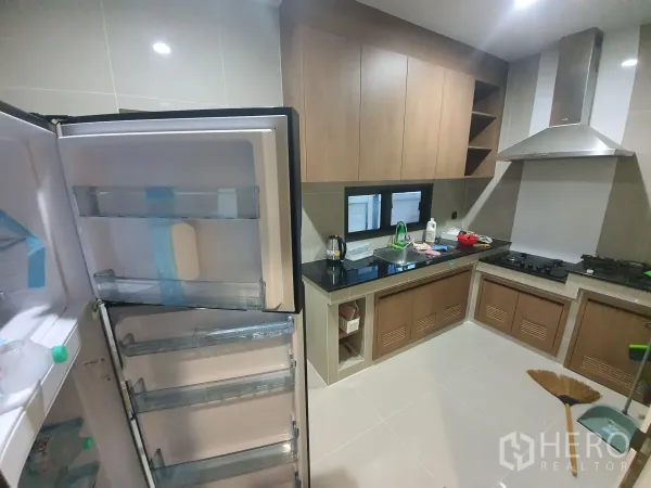 Detached House for rent in Bang Kapi, Bangkok - L-shaped closed kitchen with wood cabinets, black countertops, hob and hood.