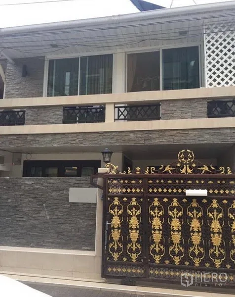 Townhouse for rent in Khlong Toei, Bangkok - Two-story Bangkok townhouse with stone-clad facade, balcony railings, and ornate gold security gate.