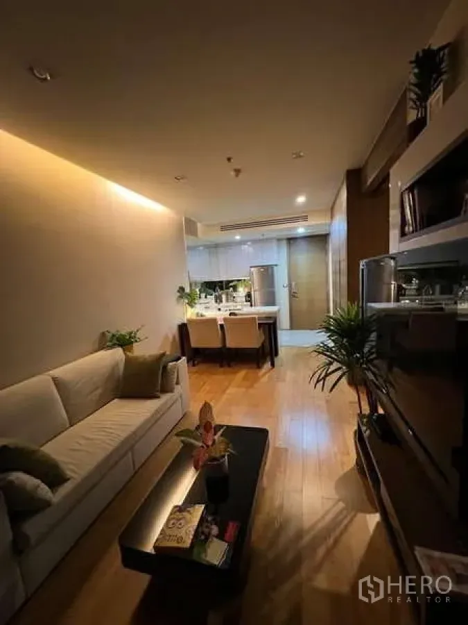 Condominium for rent in Bang Rak, Bangkok - Warm-lit lounge with sofa, TV wall unit and wood flooring.