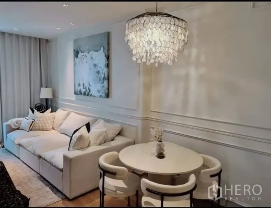 Condominium for sale in Khlong Toei, Bangkok - Wide view of living room with sofa, round dining set, and shell chandelier.