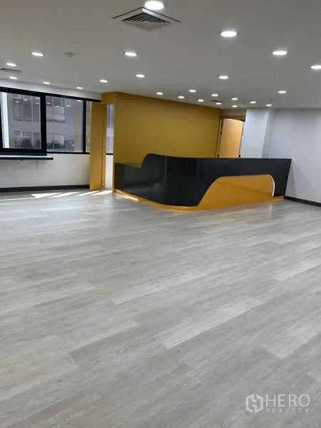 Office Space for rent in Khlong Toei, Bangkok - Modern reception with curved black-and-yellow counter and wood-look floors under downlights.