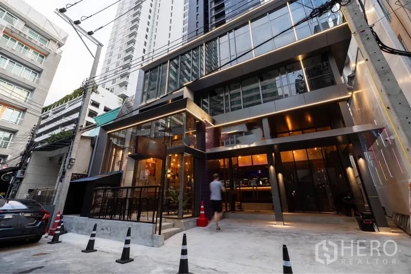 Retail Space for rent in Watthana, Bangkok - Modern glass-front commercial building exterior with warm lighting and direct street access in a lively urban lane.