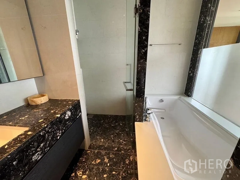 Condominium for rent - Modern bathroom featuring a black marble vanity, separate glass shower and a white soaking bathtub.