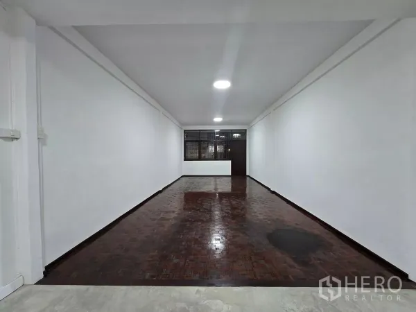 Shophouse for rent in Watthana, Bangkok - Long retail hall at night with wood parquet floor and a counter near the rear.
