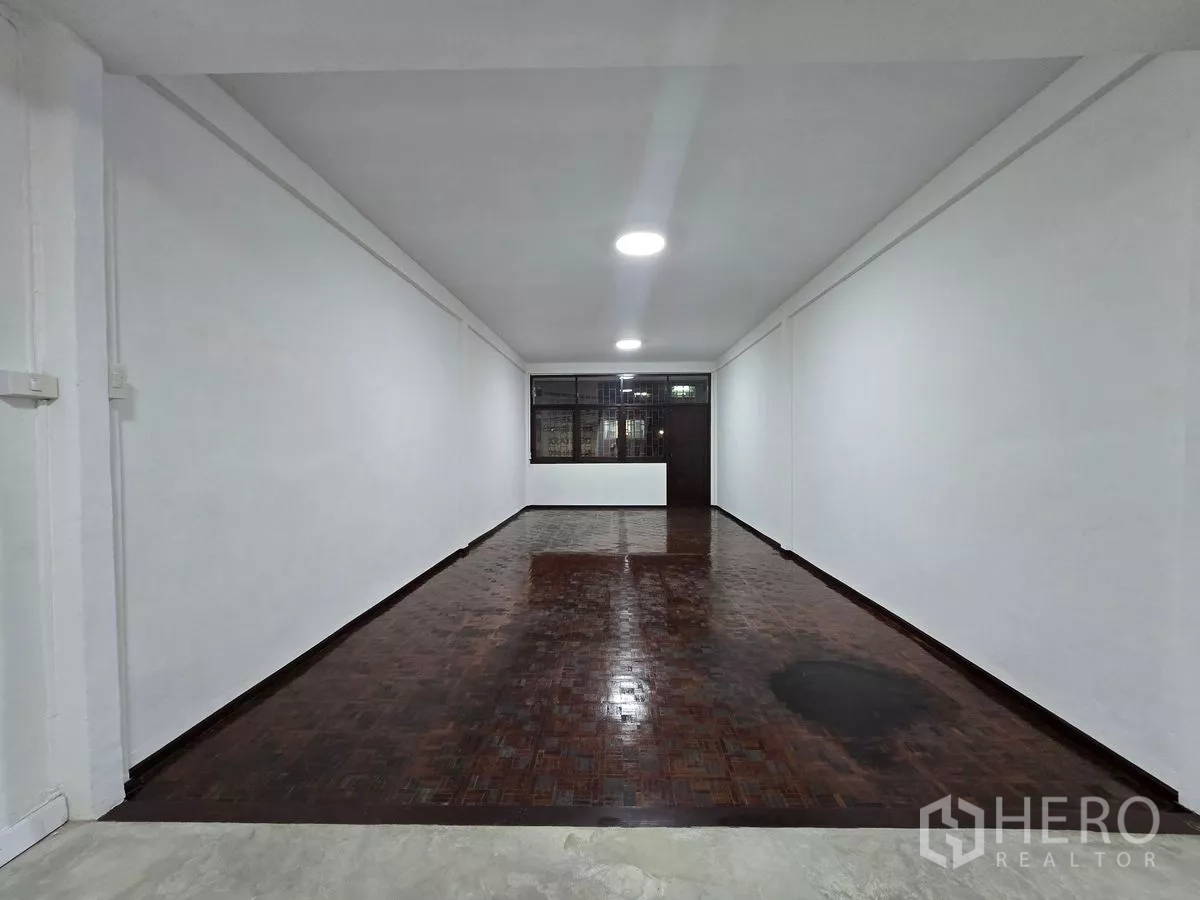 Shophouse for rent in Watthana, Bangkok - Long retail hall at night with wood parquet floor and a counter near the rear.