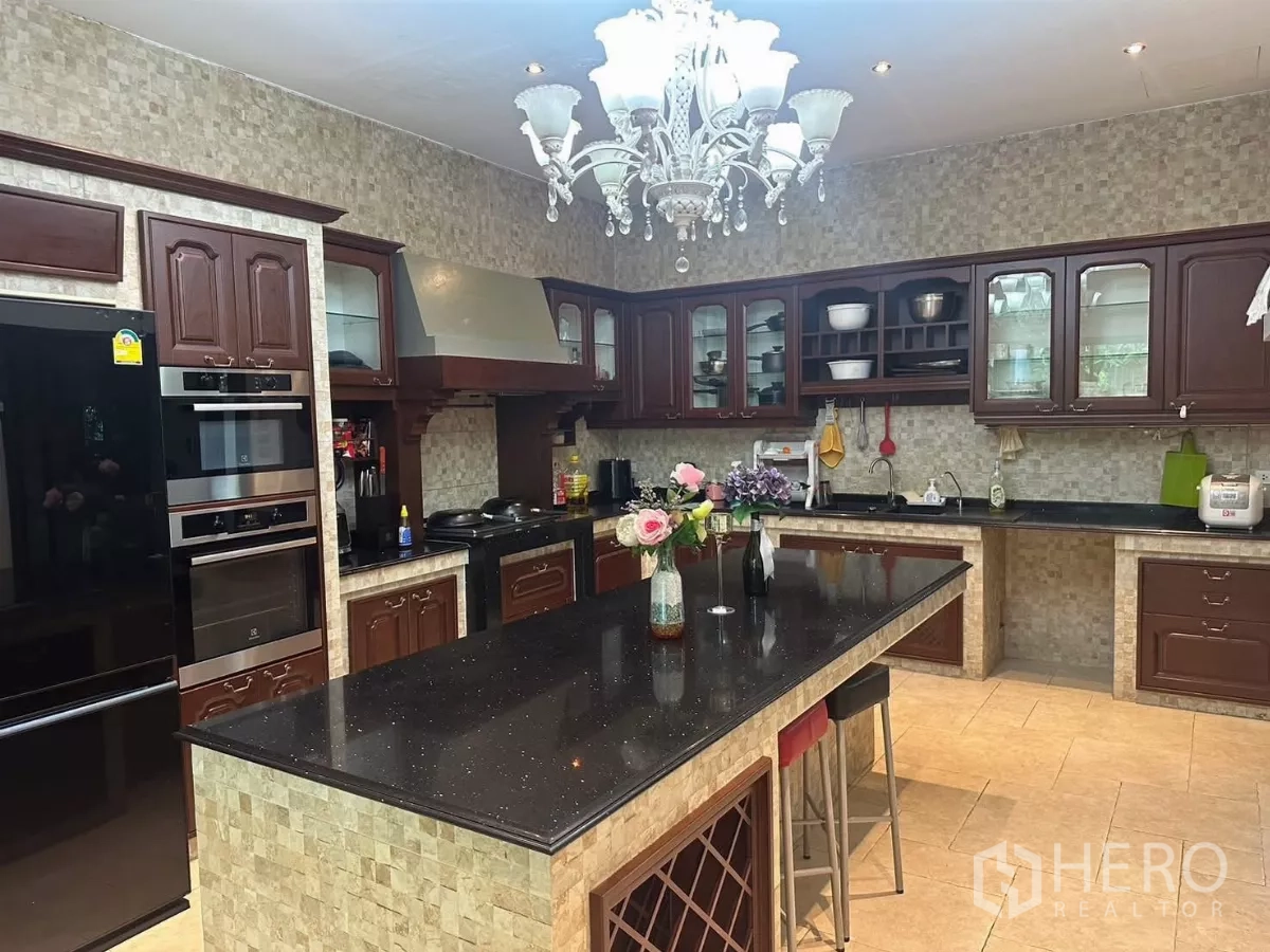 Detached House for rent or sale in Bang Kapi, Bangkok - Western kitchen with island, dark granite countertops and wooden cabinetry.