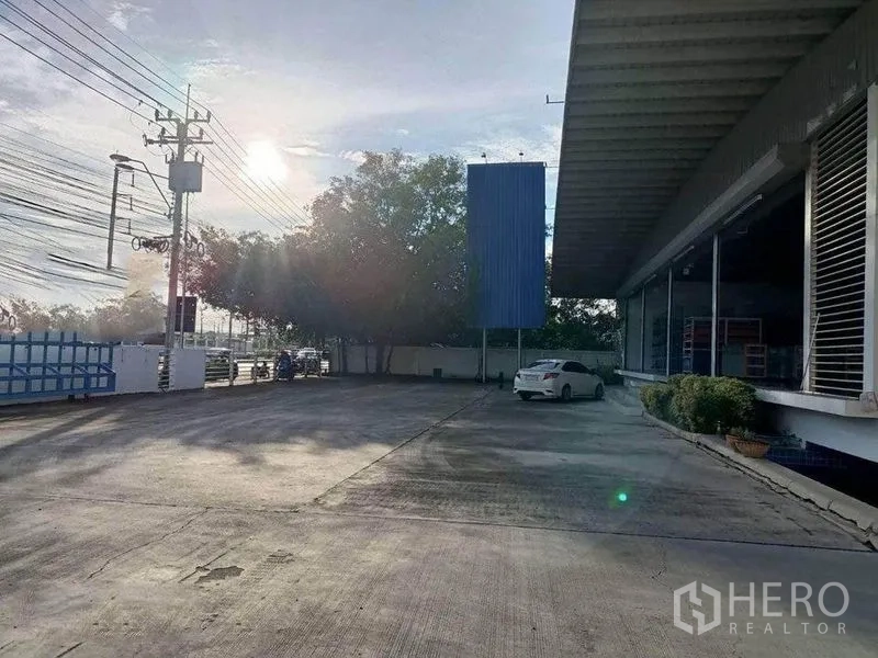 Warehouse for rent in Bang Phli, Samut Prakan - Expansive front yard and parking area with perimeter fence and long roof canopy.