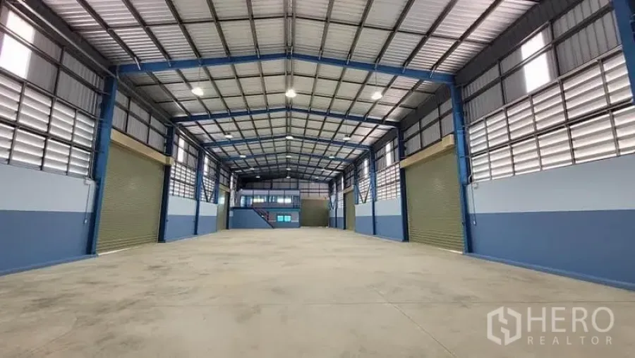 Factory for rent or sale in Phanat Nikhom, Chon Buri - Spacious high-ceiling factory hall with a steel frame, bright lighting, and multiple roller shutter doors.