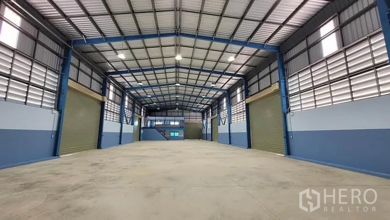 Factory for rent or sale in Phanat Nikhom, Chon Buri - Spacious high-ceiling factory hall with a steel frame, bright lighting, and multiple roller shutter doors.