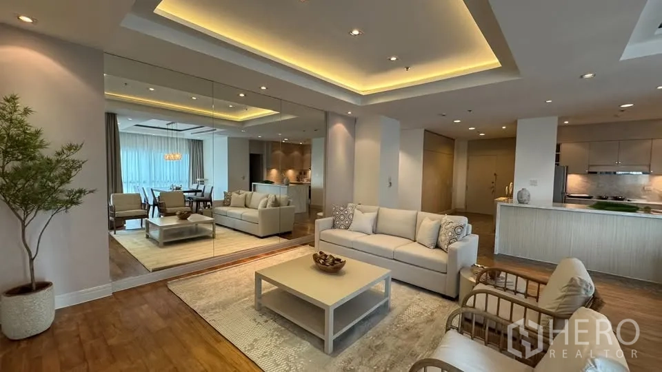 公寓 for rent in Pathum Wan, Bangkok - 开放式客餐厅，成套沙发与茶几，大幅镜面墙、嵌灯照明，旁连带操作台的厨房。