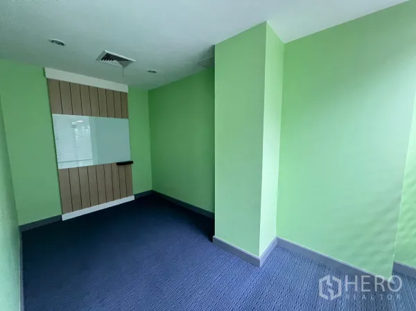 Retail Space for rent - Compact room with green walls, carpet flooring and a wall-mounted whiteboard panel.