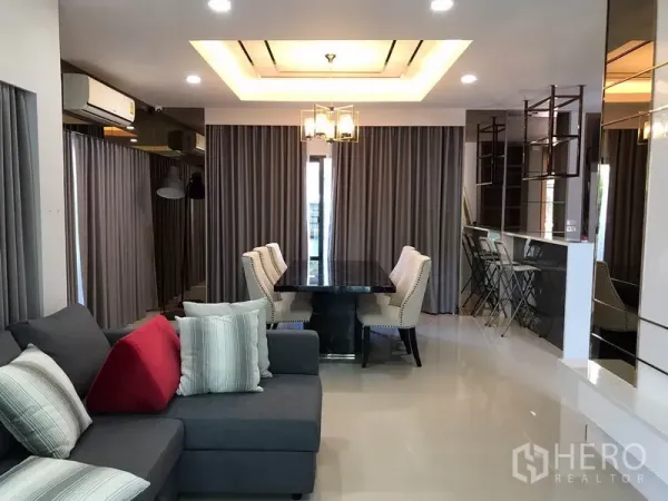 独立式住宅 出租在Bang Phli, Samut Prakan - 开放式客餐厅，托盘天花、吊灯与六人餐桌，玻璃门通向室外。